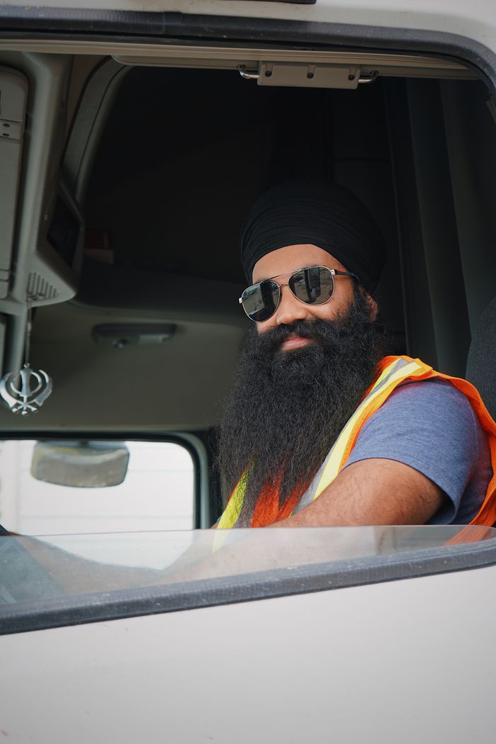 services-01 Confident truck driver wearing sunglasses and a turban, posing in vehicle cabin.
