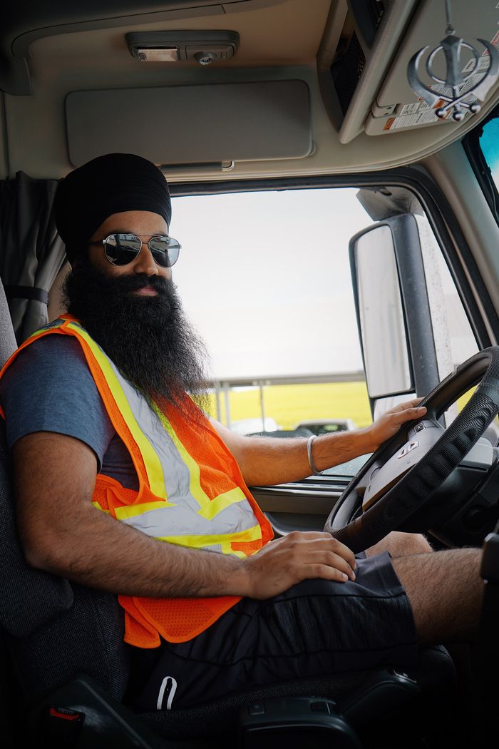 about-01 Sikh truck driver in a safety vest confidently steering a truck, capturing a professional and safety-conscious moment.
