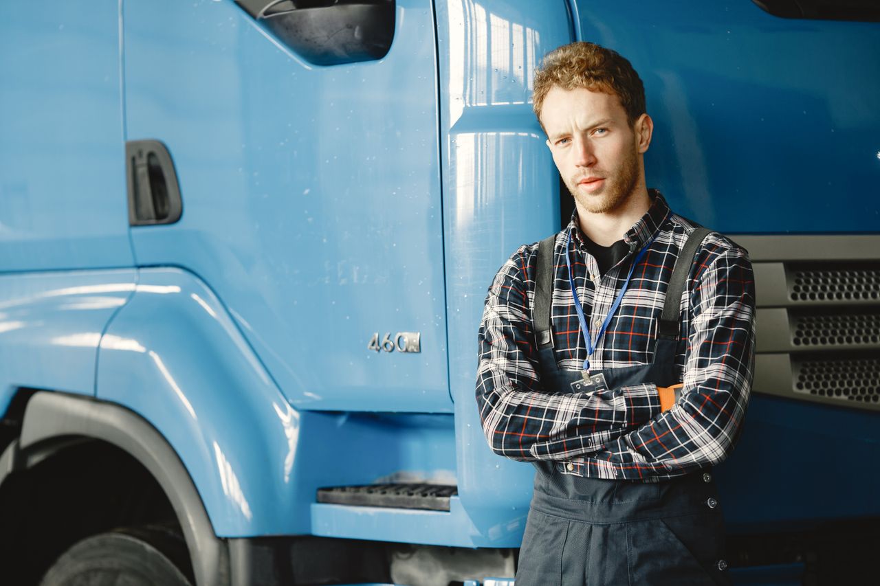 why-choose-us Auto mechanic with crossed arms posing by a blue truck in a garage